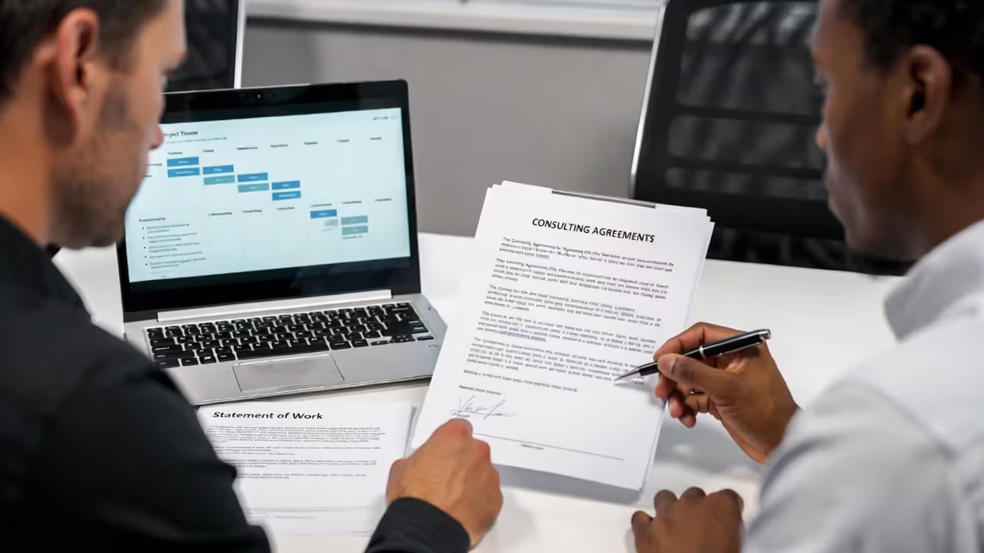 Consultant and client signing a consulting agreement at a table with scope-of-work documents