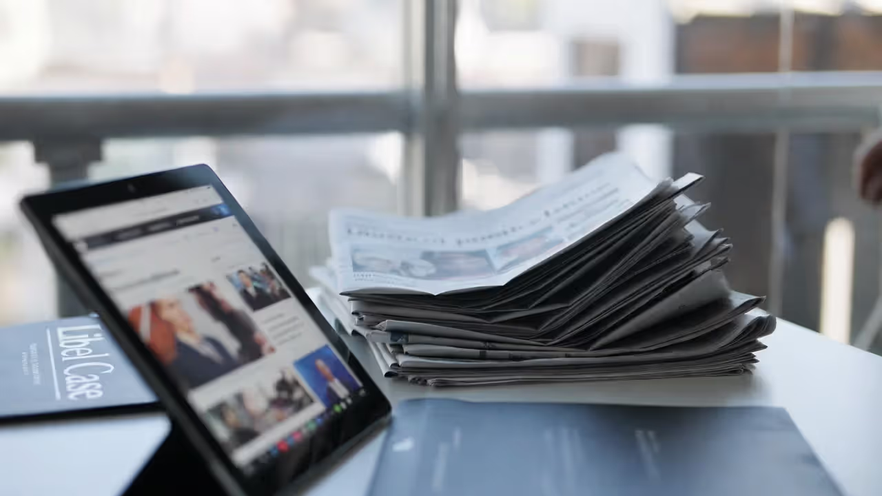 Newspapers and tablet with blurred headlines beside a libel case file