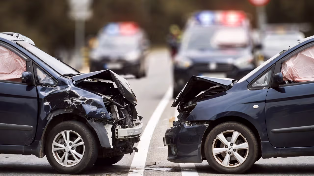 Two damaged vehicles after a traffic collision with emergency lights in background